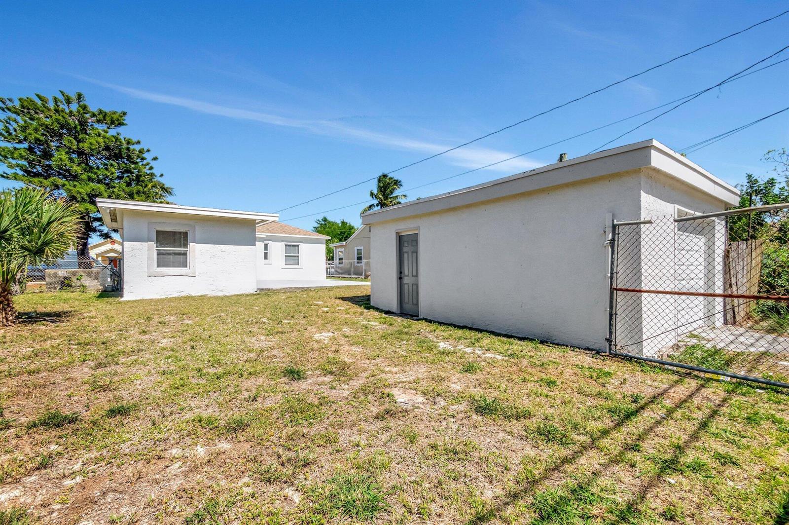 A backyard view shows a detached white garage and a small house under a blue sky — 950 29th Street, West Palm Beach FL 33407, WEST PALM BEACH, FL