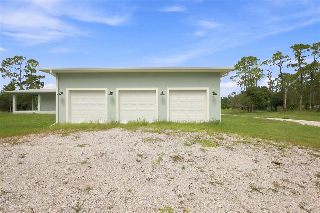 A light green detached three-car garage sits on a gravel driveway in a grassy yard — 8146 TROPICAIRE BOULEVARD, NORTH PORT, FL