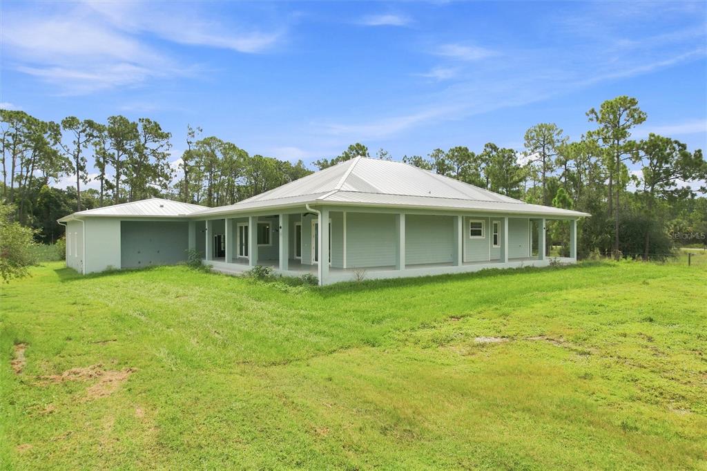 A light green house with a metal roof and a wrap-around porch sits on grass — 8146 TROPICAIRE BOULEVARD, NORTH PORT, FL