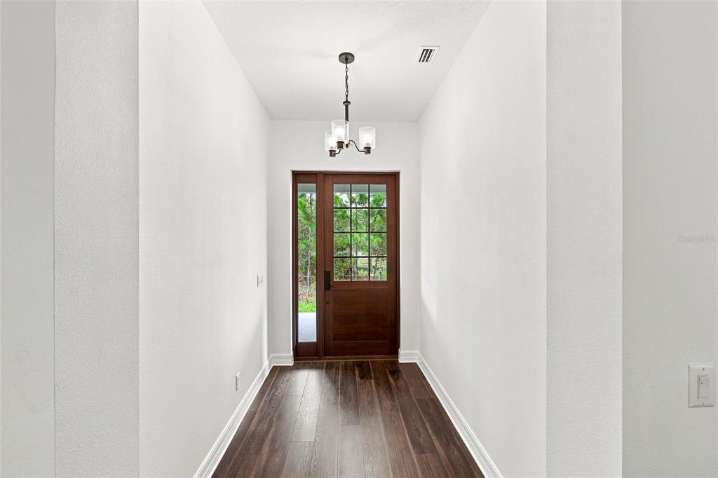 A bright entryway features dark wood flooring, white walls, and a wooden front door with glass panes — 8146 TROPICAIRE BOULEVARD, NORTH PORT, FL