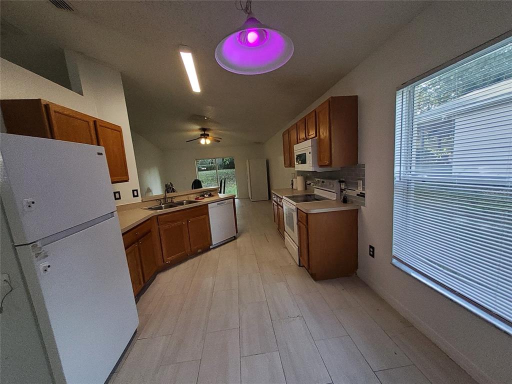 A kitchen features wood cabinets, white appliances, and light-colored tile flooring — 449 HEATHER HILL BOULEVARD, DAVENPORT, FL