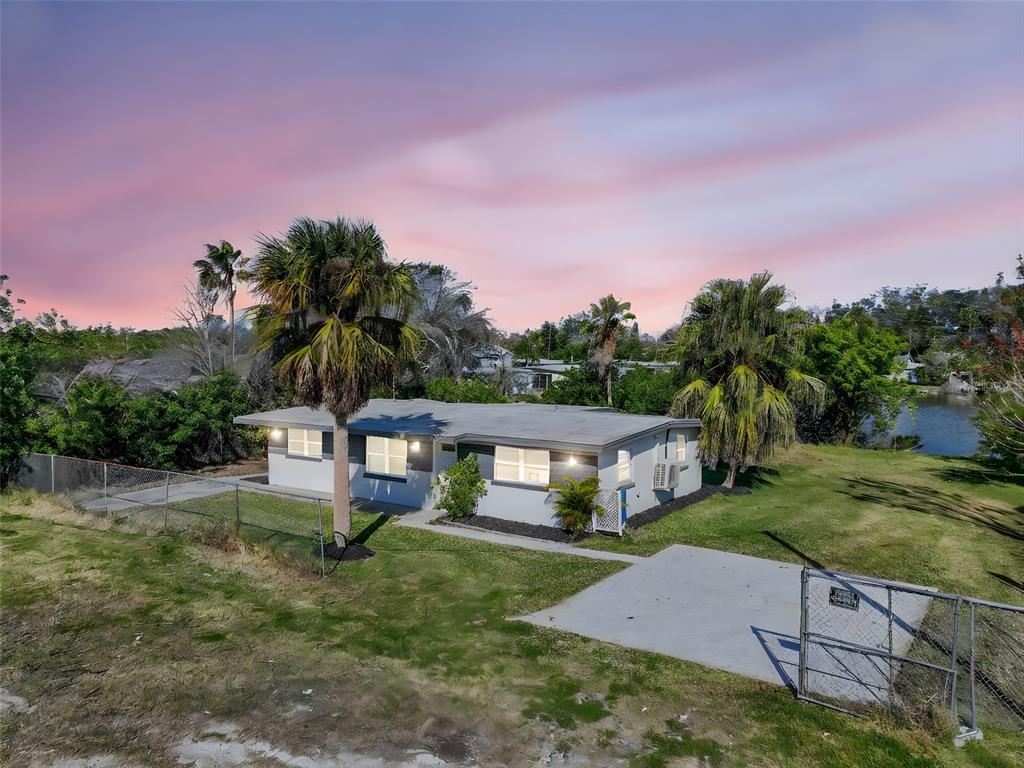 An exterior view of a single-story house with palm trees and a fenced yard — 4505 COTTONWOOD DRIVE, NEW PORT RICHEY, FL