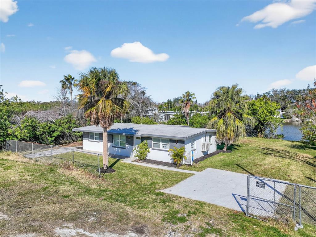 A single-story house with a flat roof, palm trees, and a fenced yard near water — 4505 COTTONWOOD DRIVE, NEW PORT RICHEY, FL