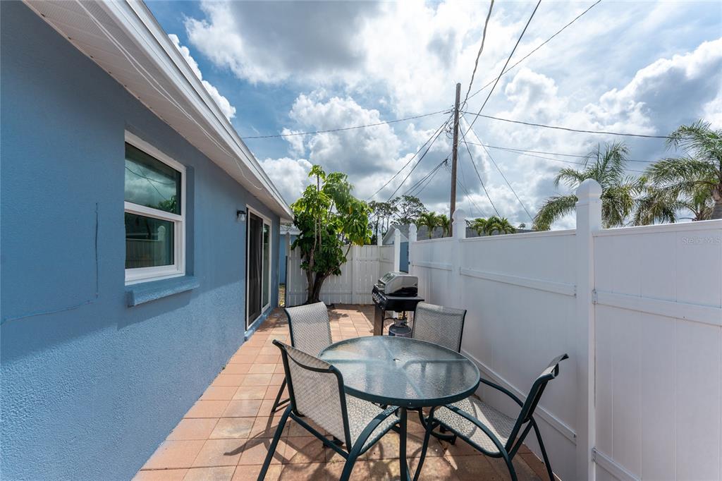 A patio with a glass-topped table and chairs sits beside a blue house exterior — 1965 LOUISIANA AVENUE, ENGLEWOOD, FL