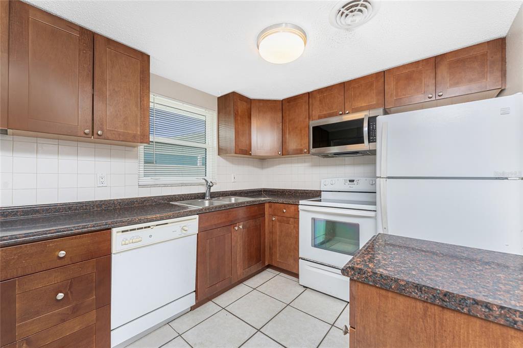 A kitchen with wood cabinets, white appliances, a tiled floor, and dark granite countertops — 1965 LOUISIANA AVENUE, ENGLEWOOD, FL