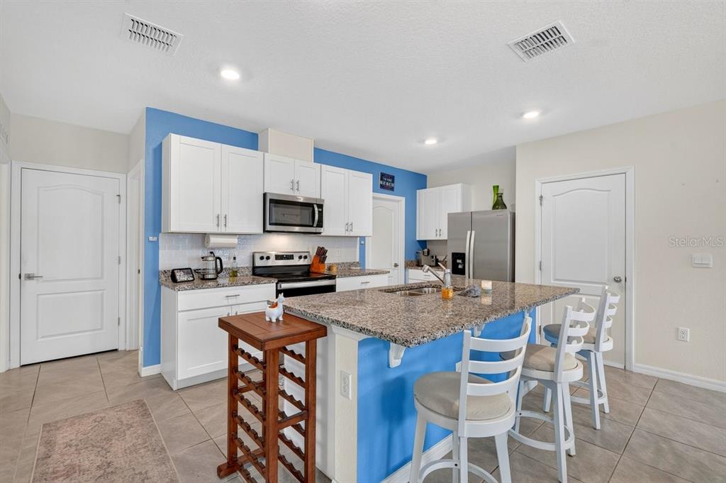 A kitchen features blue walls, white cabinets, granite countertops, and a central island with seating — 2757 PORTADOWN STREET, ORMOND BEACH, FL