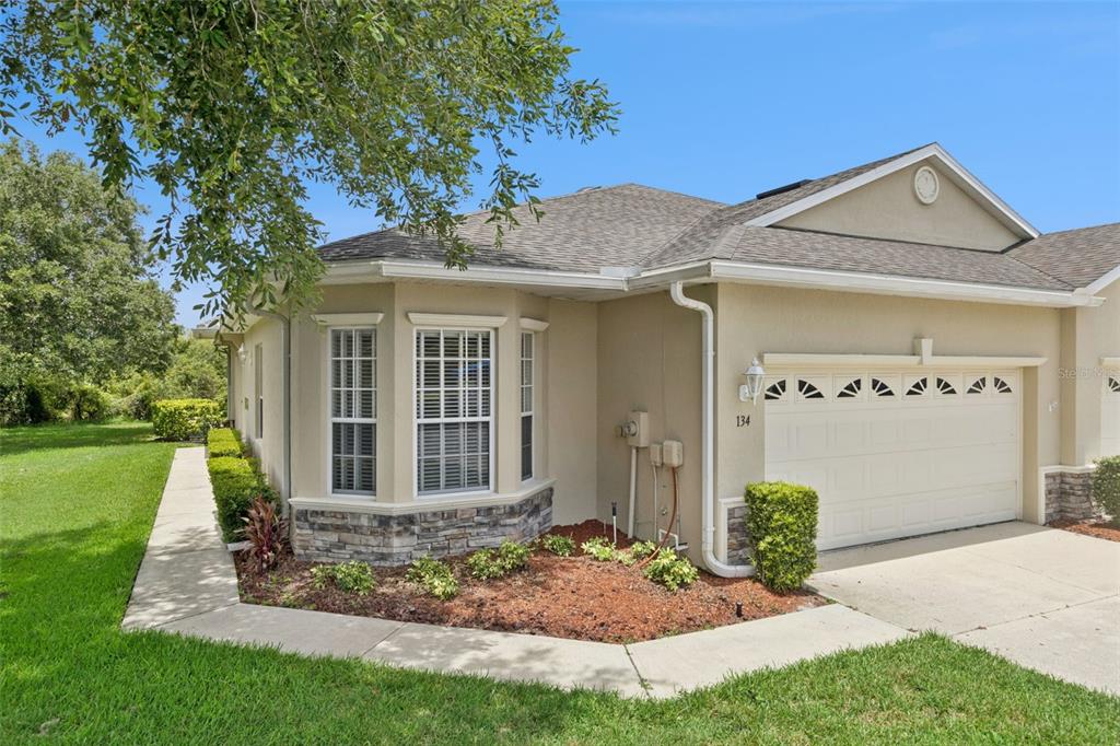 A single-story house with a beige stucco exterior, a stone-accented bay window, and a garage — 134 LOWER LAKE COURT, DEBARY, FL