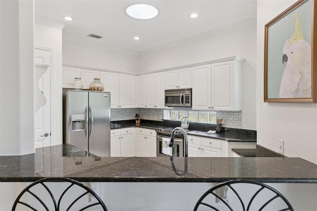 A kitchen features white cabinets, dark granite countertops, stainless steel appliances, and a breakfast bar — 134 LOWER LAKE COURT, DEBARY, FL