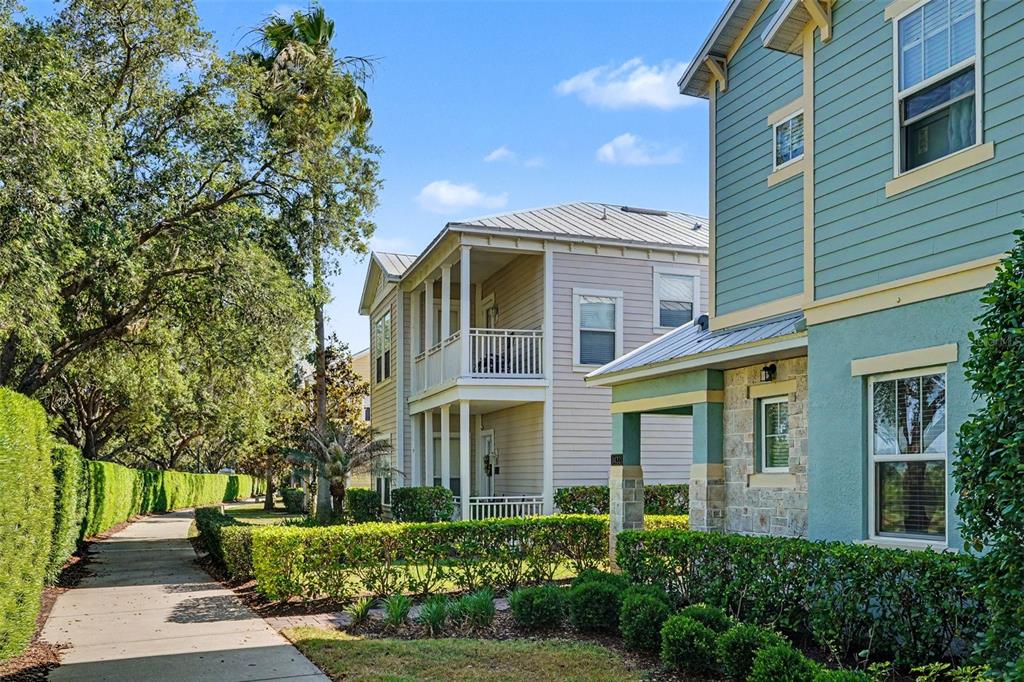 A sidewalk runs past a manicured hedge and two multi-story houses under a blue sky — 1432 REUNION BOULEVARD, REUNION, FL