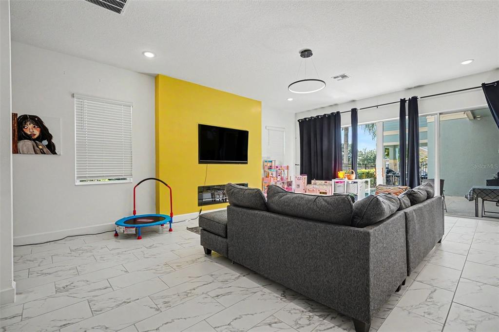 A living room features a yellow accent wall, a gray sectional sofa, and tile flooring — 1432 REUNION BOULEVARD, REUNION, FL