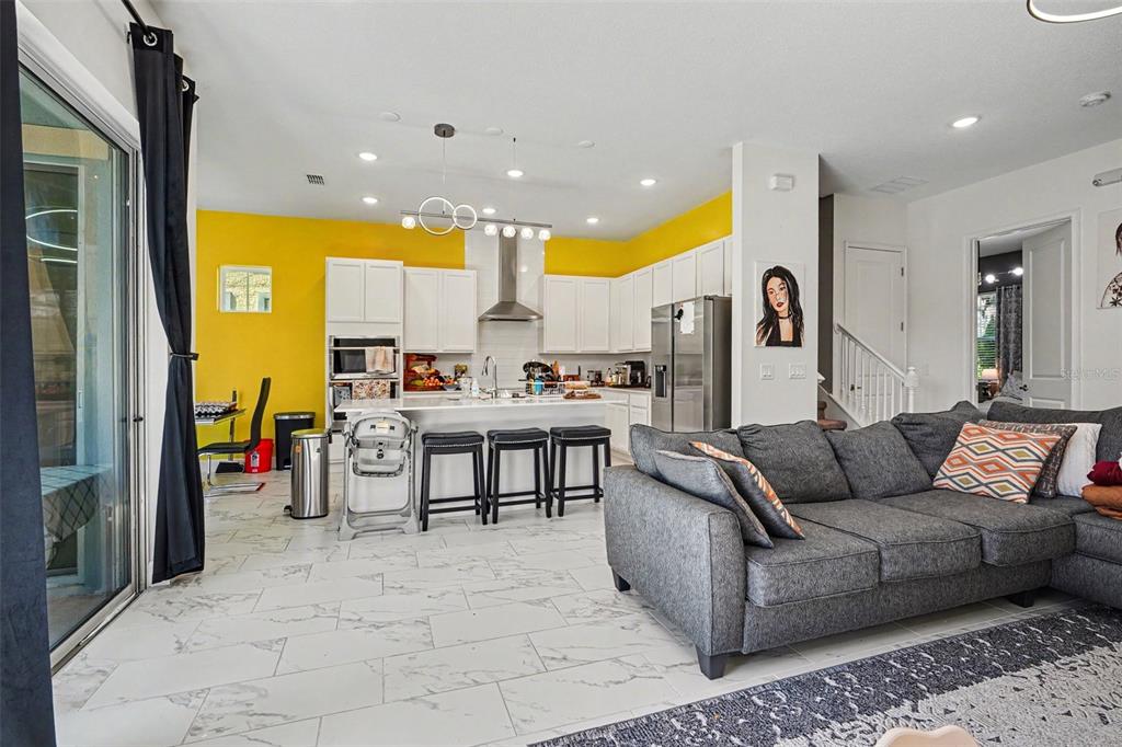 An open-concept kitchen and living area features white cabinets, yellow walls, and marble-look tile flooring — 1432 REUNION BOULEVARD, REUNION, FL