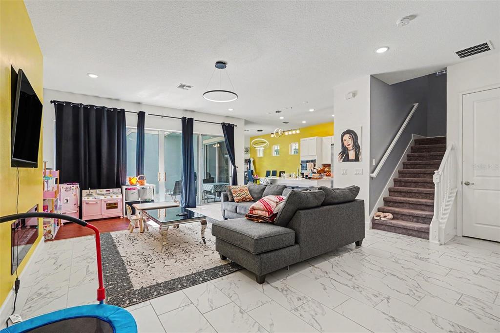 A living room features white tile floors, a grey sectional sofa, and a yellow accent wall — 1432 REUNION BOULEVARD, REUNION, FL