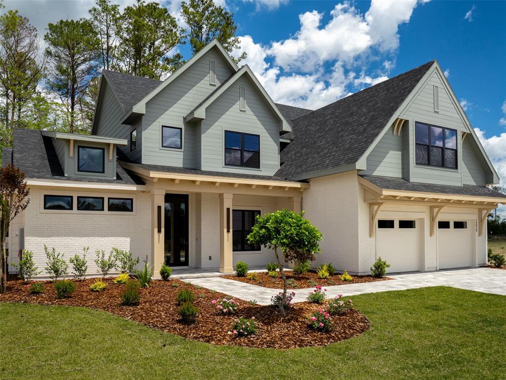 A two-story house features white brick, sage green siding, a dark roof, and a front porch — 14828 SW 9TH LANE, NEWBERRY, FL