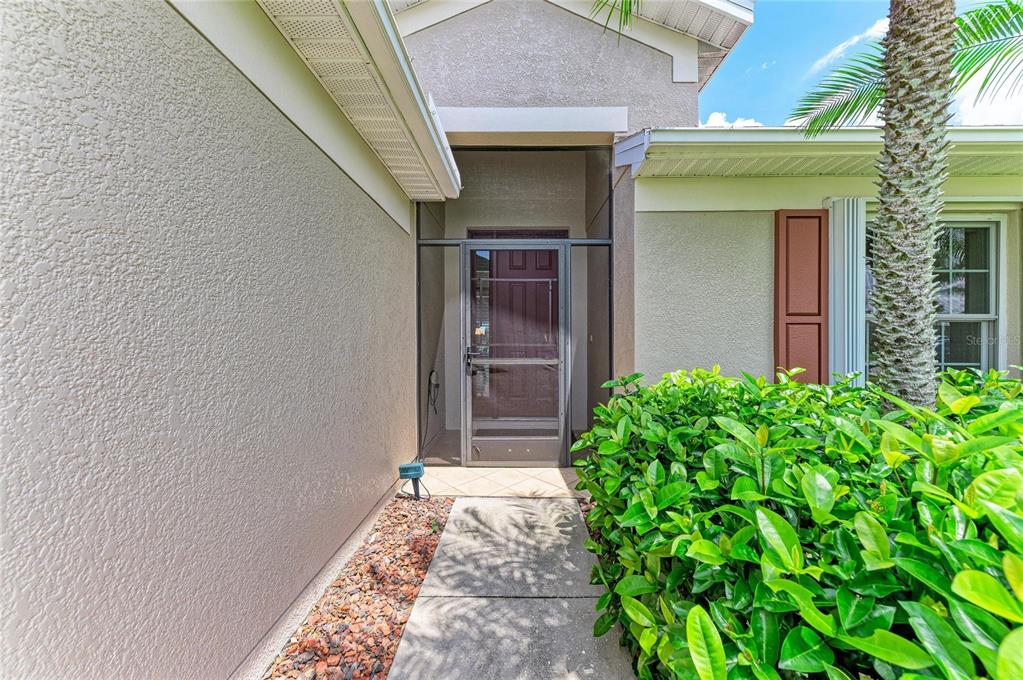 A concrete walkway leads to a front entrance with a screen door and landscaping — 9882 50TH STREET CIRCLE E, PARRISH, FL
