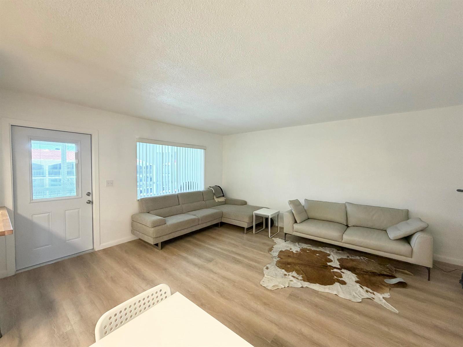 A living room features light wood flooring, two sofas, a cowhide rug, and a white door — 580 Egret Drive # 305, Hallandale Beach FL 33009, HALLANDALE BEACH, FL