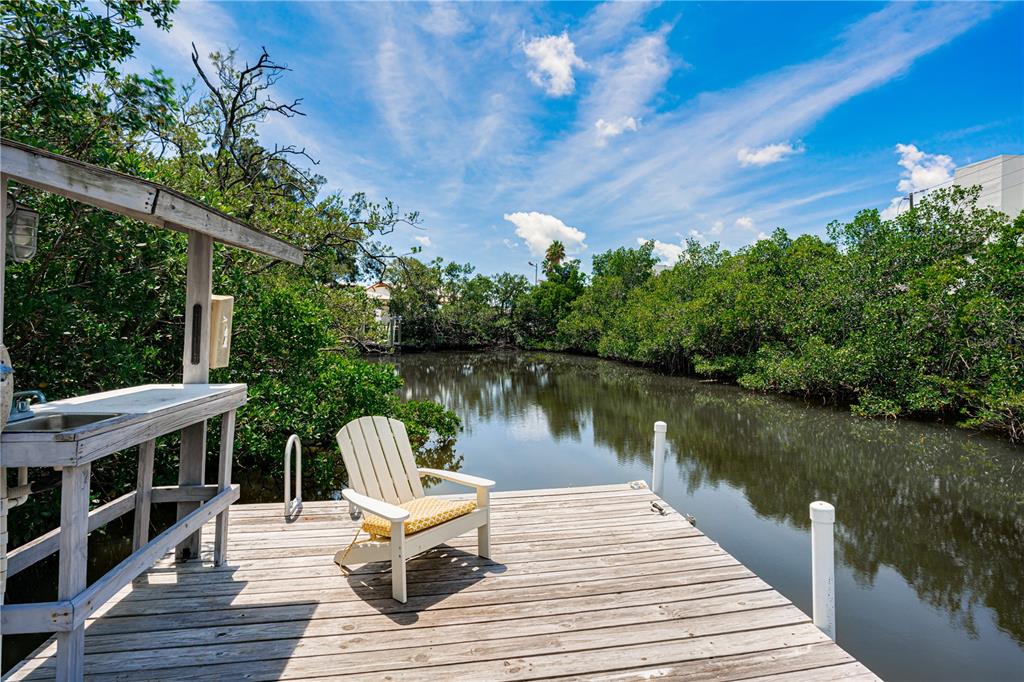 A wooden dock with a chair and cleaning station overlooks a narrow, tree-lined canal — 115 CANAL AVENUE UNIT 3, INDIAN ROCKS BEACH, FL
