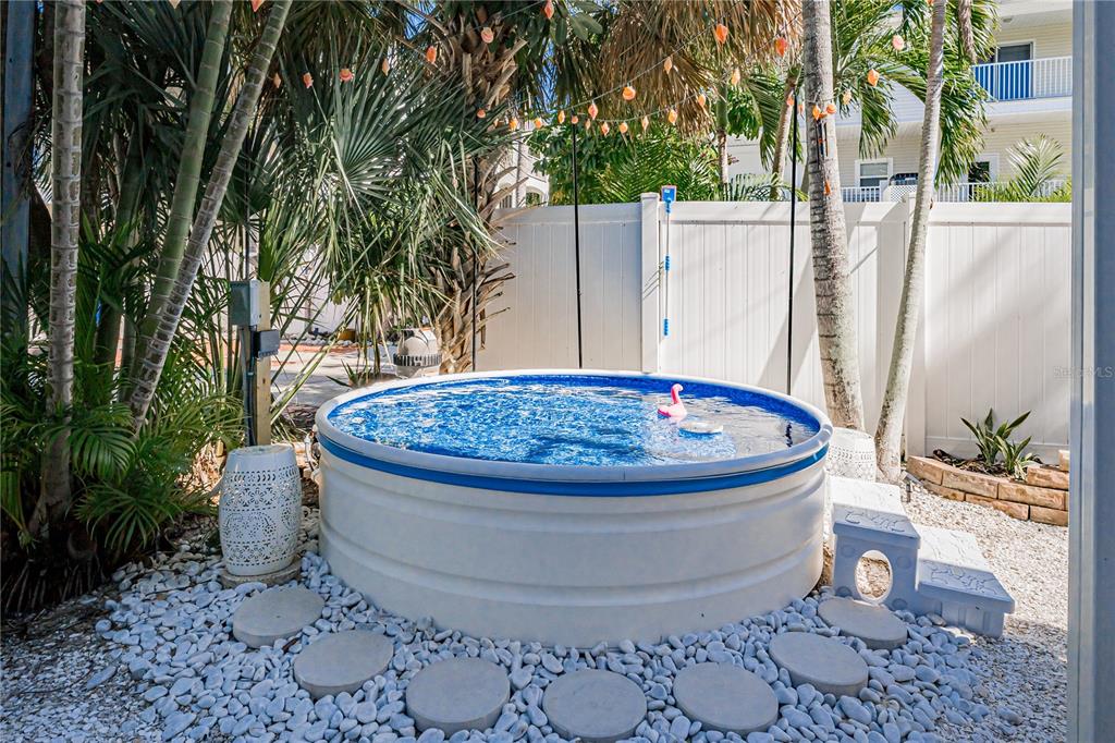 A round stock tank pool sits on a gravel patio with stepping stones and palm trees — 115 CANAL AVENUE UNIT 3, INDIAN ROCKS BEACH, FL