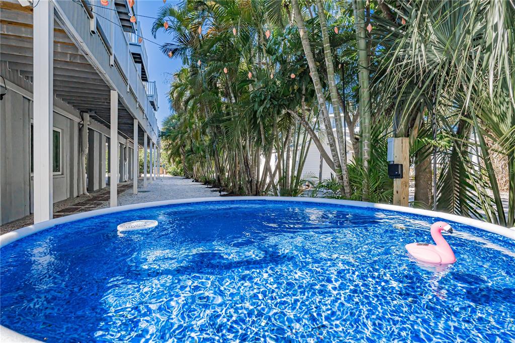 A round above-ground swimming pool sits on a gravel patio beside a stilted house — 115 CANAL AVENUE UNIT 3, INDIAN ROCKS BEACH, FL