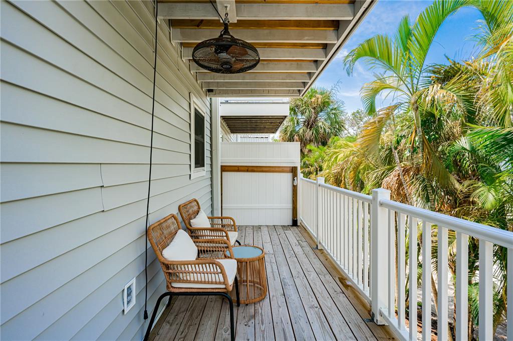 A wooden balcony features two wicker chairs, a small side table, and a ceiling fan — 115 CANAL AVENUE UNIT 3, INDIAN ROCKS BEACH, FL