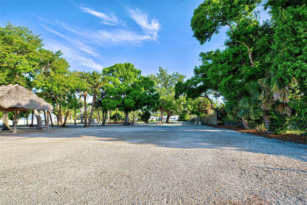A large, gravel-covered outdoor lot is surrounded by mature trees and a thatched-roof structure — 348 W DEARBORN STREET, ENGLEWOOD, FL