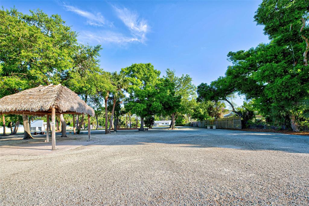 A gravel lot features a thatched-roof pavilion surrounded by mature trees and a wooden fence — 348 W DEARBORN STREET, ENGLEWOOD, FL
