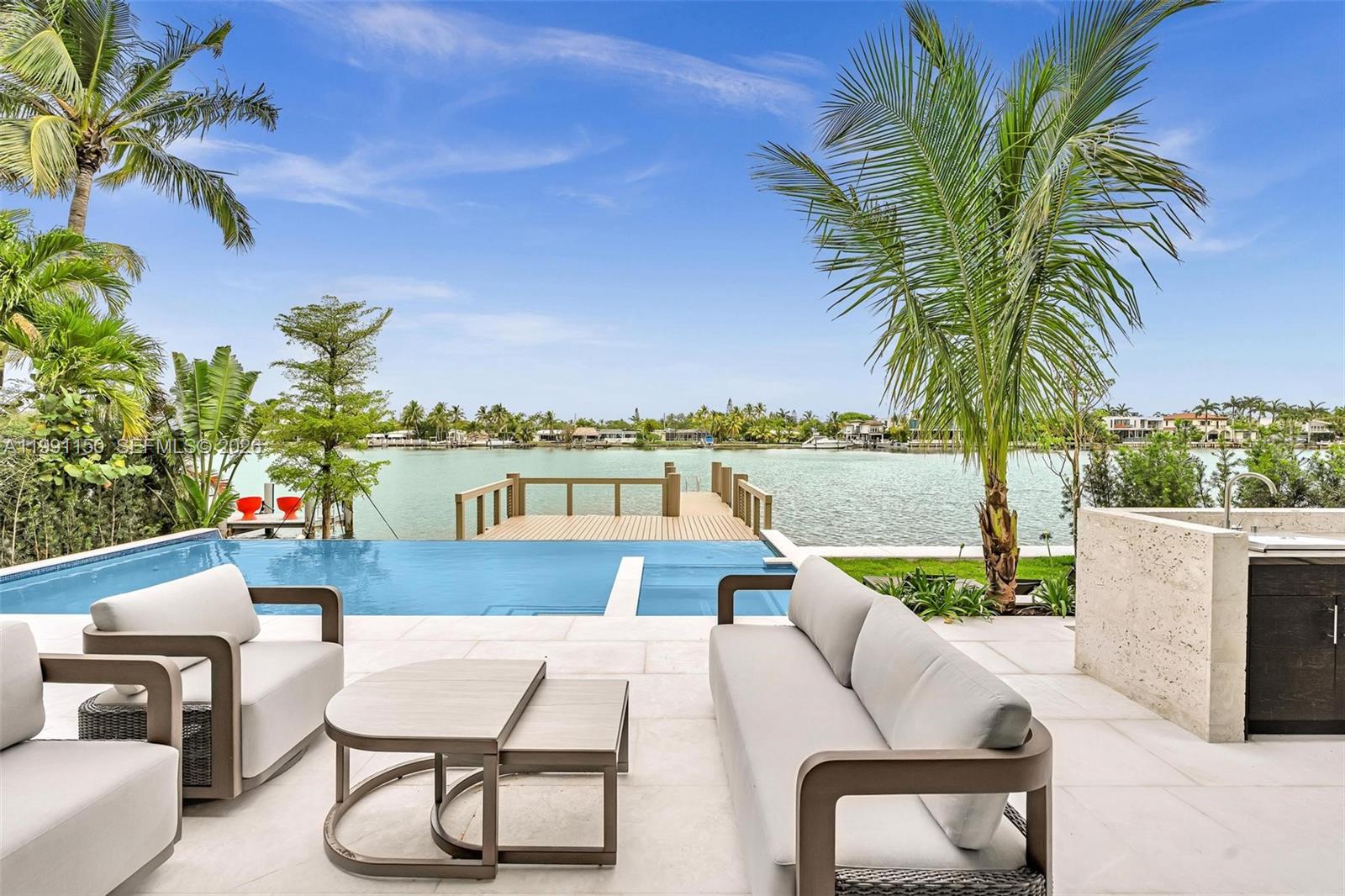 A patio with outdoor furniture overlooks an infinity pool, a wooden dock, and a waterway — 535 N Shore Dr, Miami Beach FL 33141, MIAMI BEACH, FL
