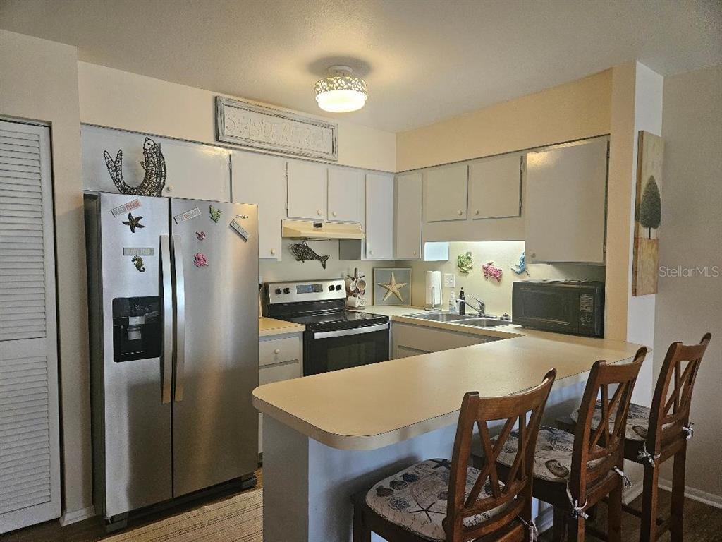 A kitchen features stainless steel appliances, light-colored cabinets, a breakfast bar, and coastal-themed decor — 810 KINGS COURT UNIT B, PUNTA GORDA, FL