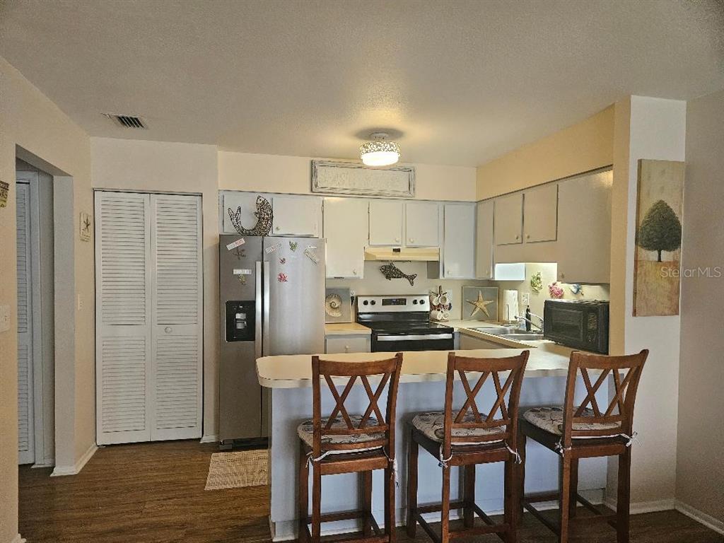 A kitchen features light-colored cabinets, stainless steel appliances, and a breakfast bar with three chairs — 810 KINGS COURT UNIT B, PUNTA GORDA, FL