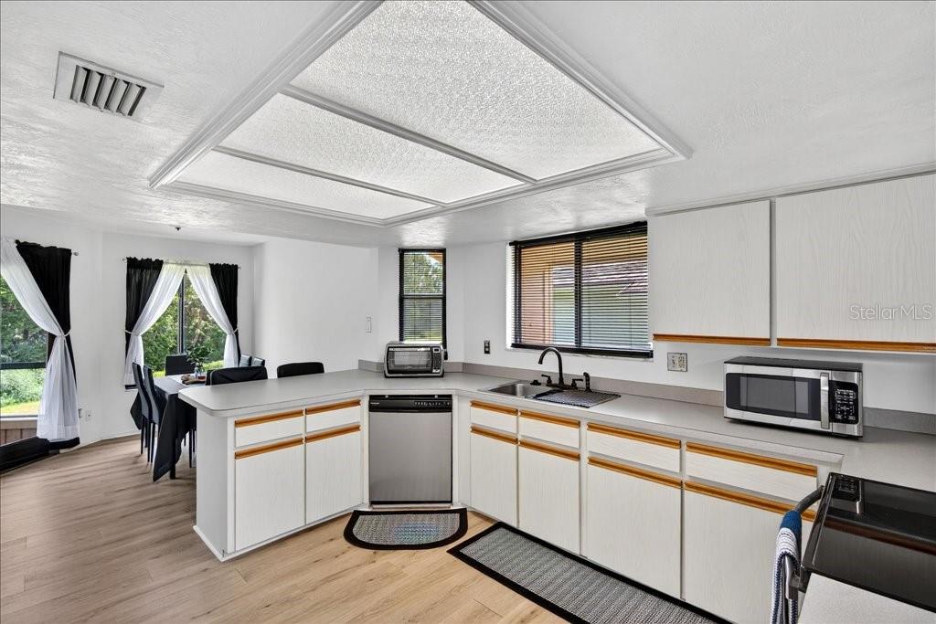 A kitchen with white cabinets, wood trim, light countertops, and a large recessed ceiling light — 133 BLUE HERON DRIVE UNIT D, DAYTONA BEACH, FL