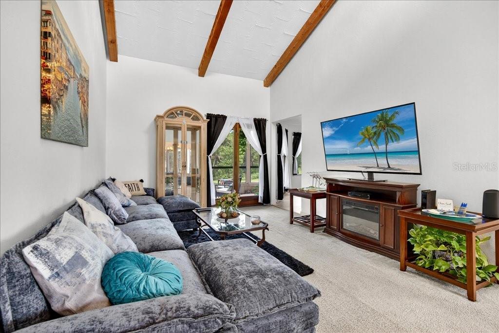 A living room features a gray sectional sofa, a television on a console, and wood beams — 133 BLUE HERON DRIVE UNIT D, DAYTONA BEACH, FL