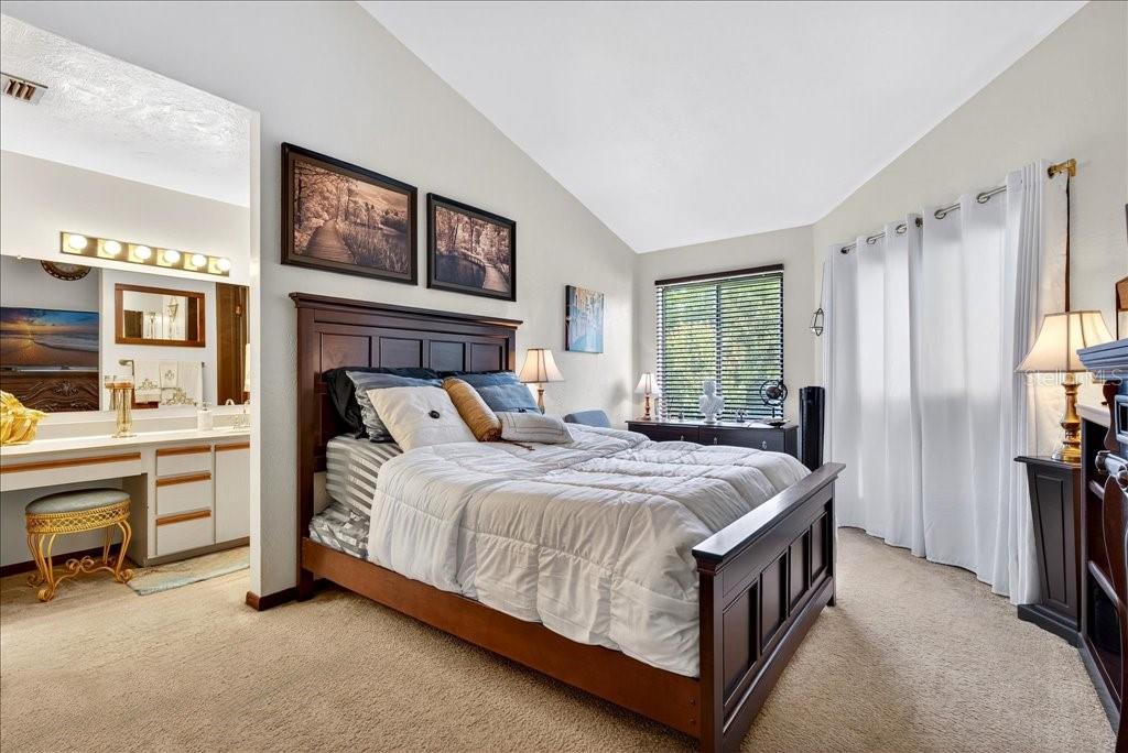 A bedroom with a dark wood bed frame, a white comforter, and an attached vanity area — 133 BLUE HERON DRIVE UNIT D, DAYTONA BEACH, FL