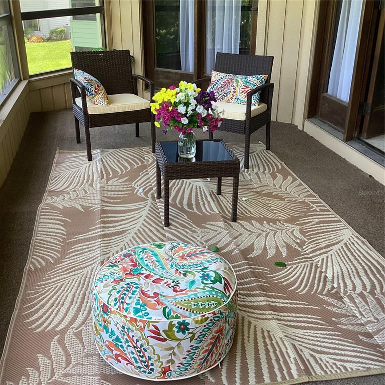 A covered patio features two wicker chairs, a small table with flowers, and a patterned rug — 133 BLUE HERON DRIVE UNIT D, DAYTONA BEACH, FL