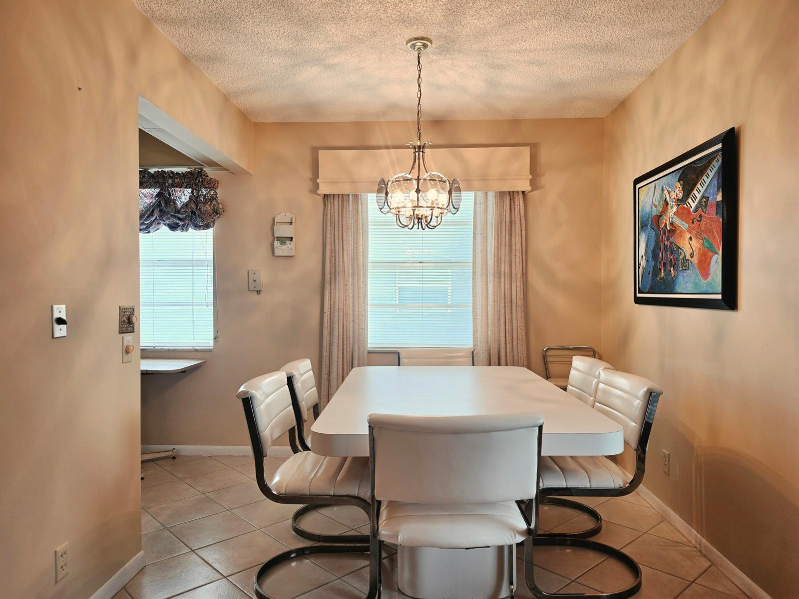 A dining room features a white table, six chairs, a chandelier, and a framed painting — 719 Flanders Drive # O, Delray Beach FL 33484, DELRAY BEACH, FL