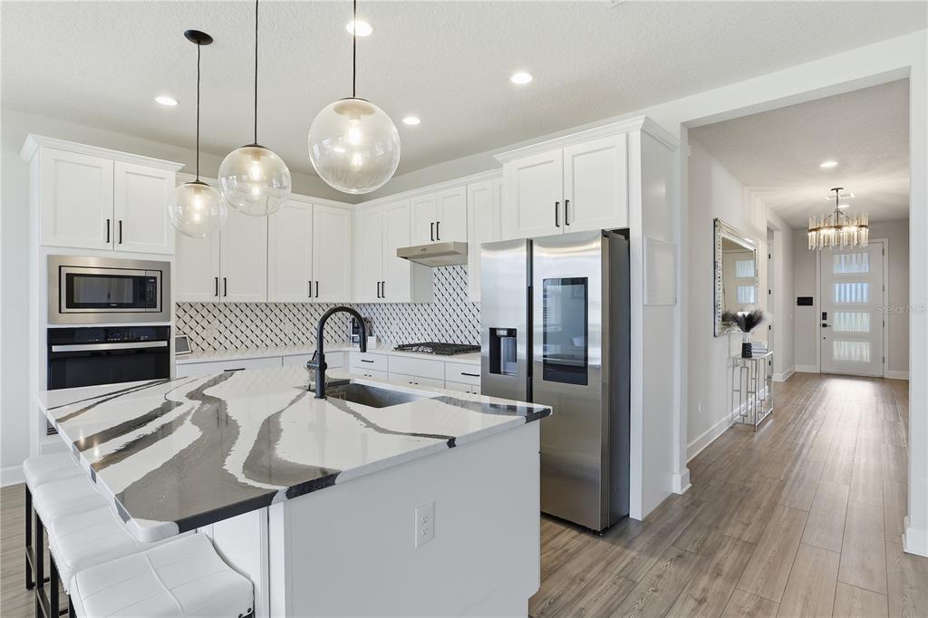 A modern kitchen features white cabinetry, a marble-patterned island, stainless steel appliances, and pendant lighting — 2784 PARK RIDGE STREET, APOPKA, FL