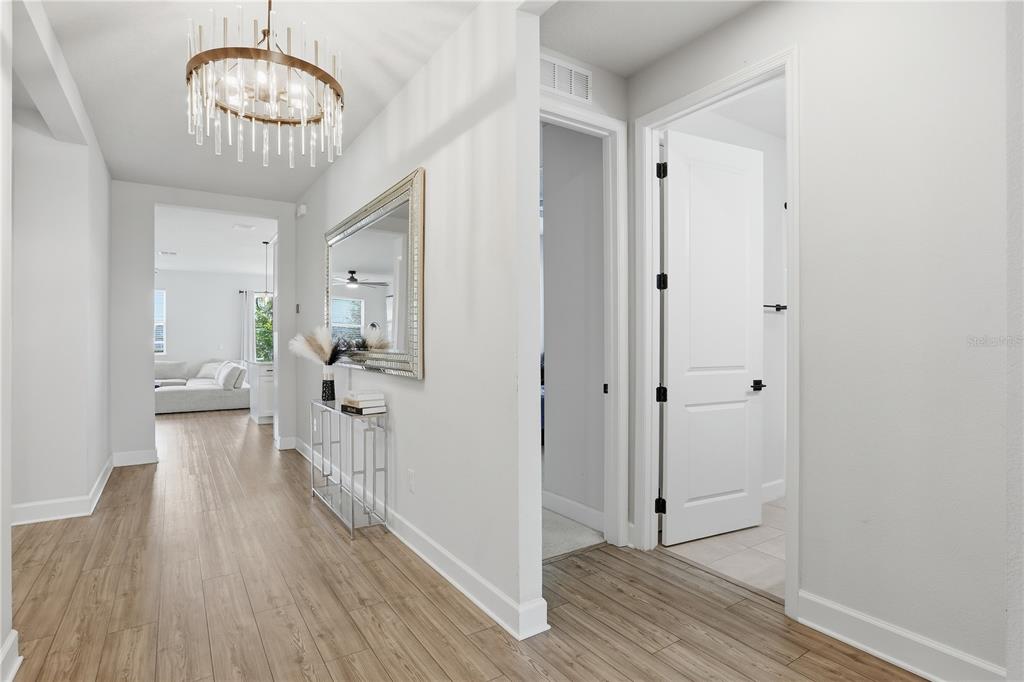 A bright hallway features light wood-look flooring, a crystal chandelier, and a console table — 2784 PARK RIDGE STREET, APOPKA, FL