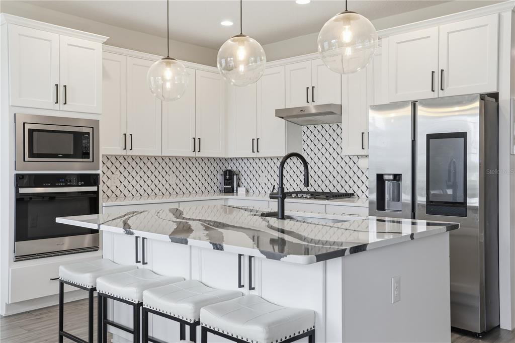 A modern kitchen features white cabinets, a large island with a marble countertop, and stainless appliances — 2784 PARK RIDGE STREET, APOPKA, FL