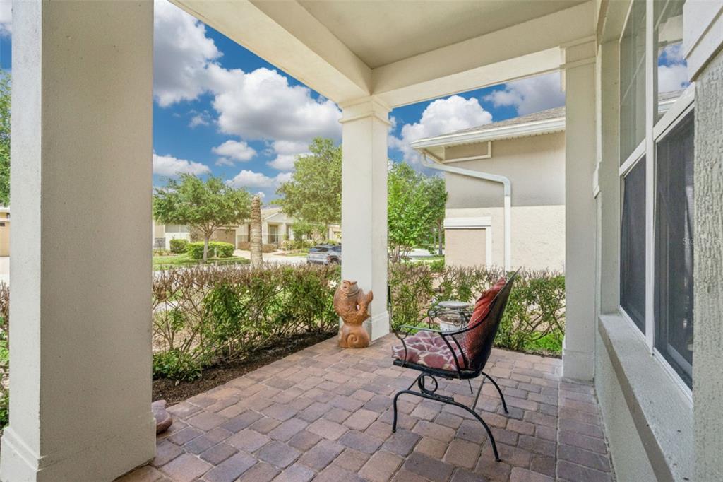 A covered patio features brick pavers, a metal chair, and a decorative sculpture — 4912 CATALPA DRIVE, ST CLOUD, FL