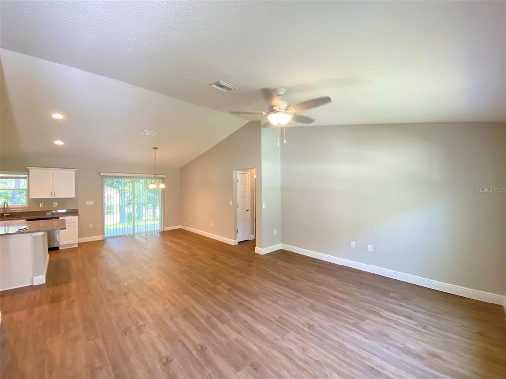 An open-concept living and dining area features vaulted ceilings, wood-look flooring, and a kitchen — 9065 N AKOLA WAY, CITRUS SPRINGS, FL