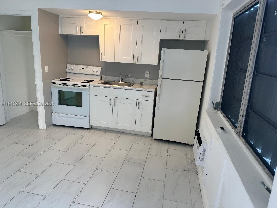 A small kitchen features white cabinets, white appliances, and light-colored tiled flooring — 1293 NE 109th St # 3, Miami FL 33161, MIAMI, FL