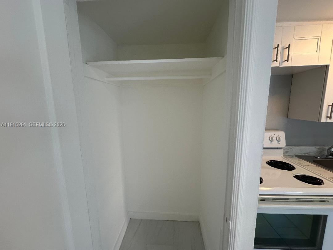 A small closet with a single shelf and hanging rod sits beside a kitchen stove — 1293 NE 109th St # 3, Miami FL 33161, MIAMI, FL