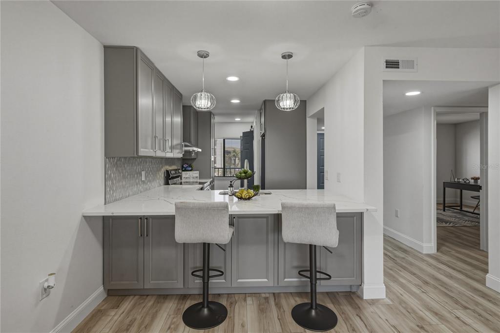 A kitchen features gray cabinets, white marble-look countertops, two bar stools, and pendant lighting — 8150 BRENT STREET UNIT 725, PORT RICHEY, FL