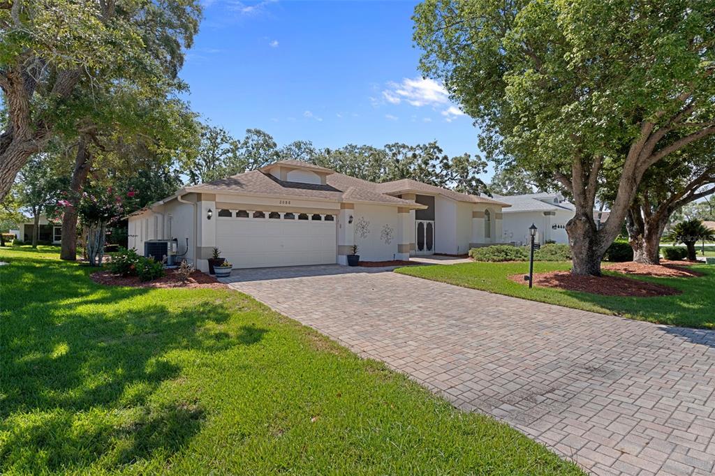 A single-story house with a paved driveway, two-car garage, and mature trees in the yard — 2086 SPARKLING WATERS WAY, SPRING HILL, FL