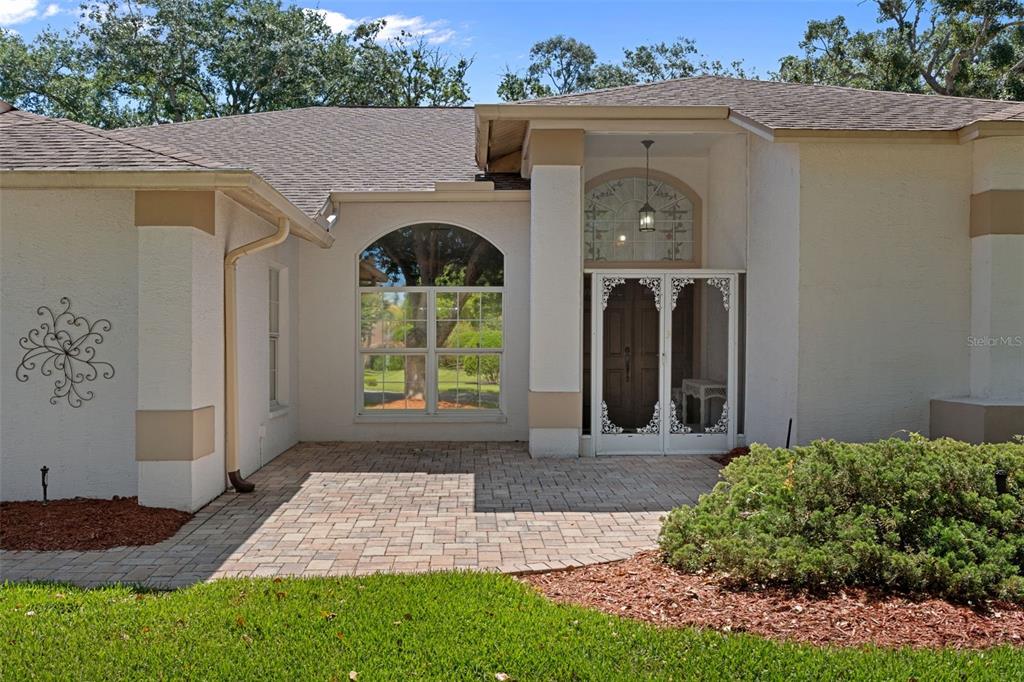 A paved patio leads to the front entrance of a house with a white exterior — 2086 SPARKLING WATERS WAY, SPRING HILL, FL