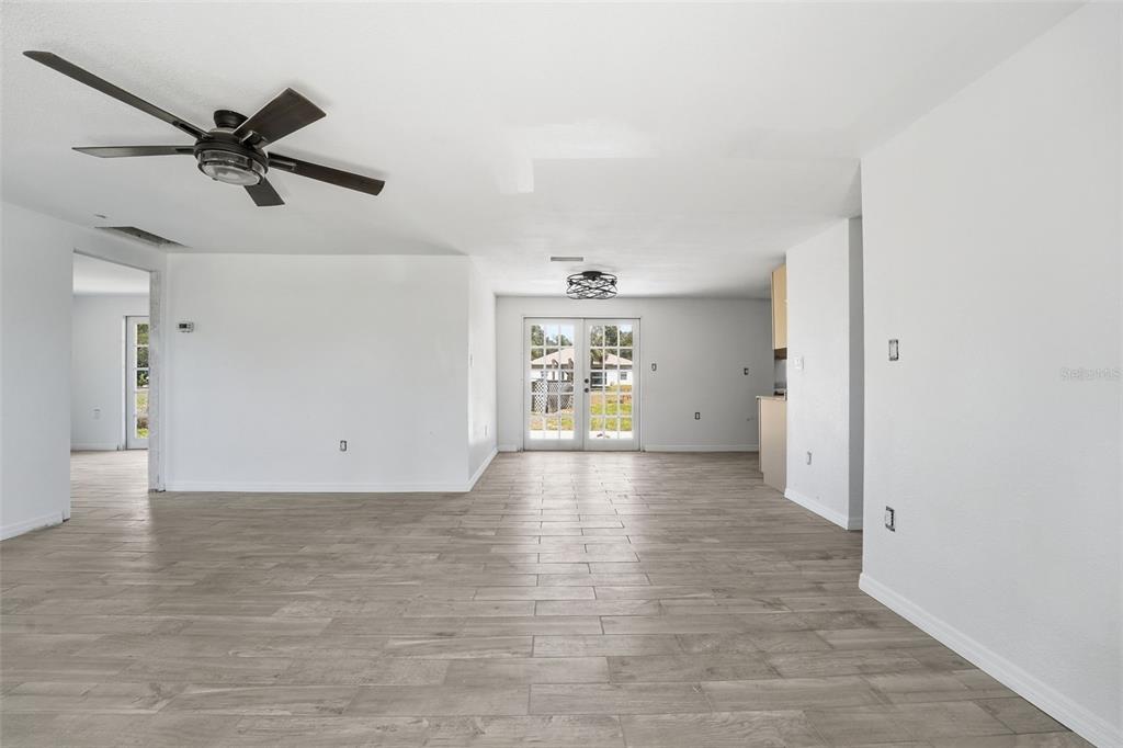 An open-concept living area with white walls, wood-look tile flooring, and French doors — 4530 CAZES AVENUE, NORTH PORT, FL