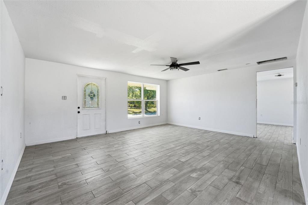 A bright living room features white walls, gray wood-look tile flooring, and a ceiling fan — 4530 CAZES AVENUE, NORTH PORT, FL