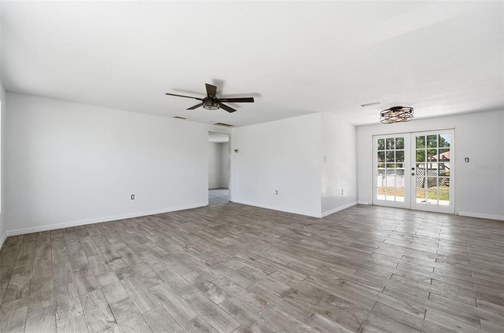 A bright, empty room features gray wood-look tile flooring, white walls, a ceiling fan, and French doors — 4530 CAZES AVENUE, NORTH PORT, FL
