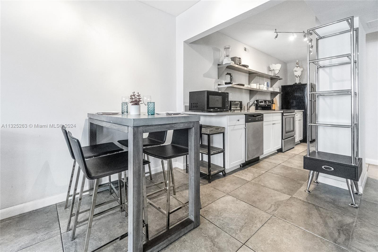 A kitchen features white cabinetry, open shelving, stainless steel appliances, and a small dining table — 100 Lincoln Rd # 320, Miami Beach FL 33139, MIAMI BEACH, FL