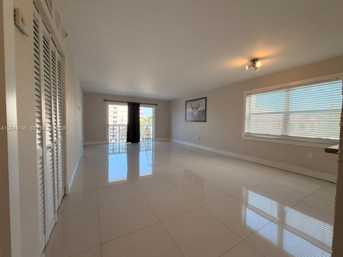 An empty living room features light-colored tile flooring, white walls, and a sliding glass door — 4141 Nautilus Dr # 4J, Miami Beach FL 33140, MIAMI BEACH, FL