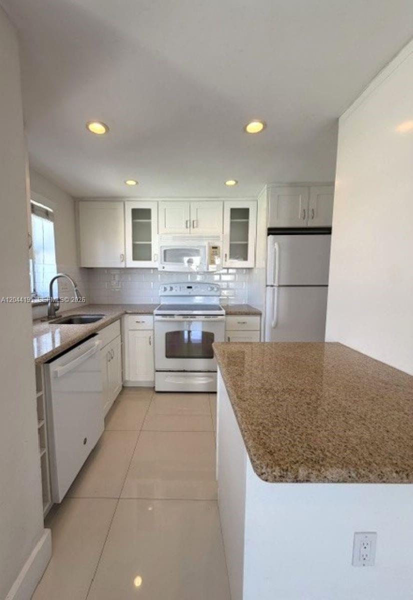 A kitchen features white cabinets, granite countertops, stainless steel appliances, and light-colored tile flooring — 4141 Nautilus Dr # 4J, Miami Beach FL 33140, MIAMI BEACH, FL
