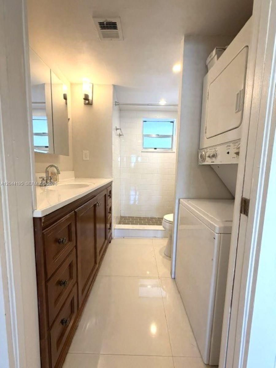 A bathroom with a wooden vanity, a walk-in shower, and a stacked washer and dryer — 4141 Nautilus Dr # 4J, Miami Beach FL 33140, MIAMI BEACH, FL